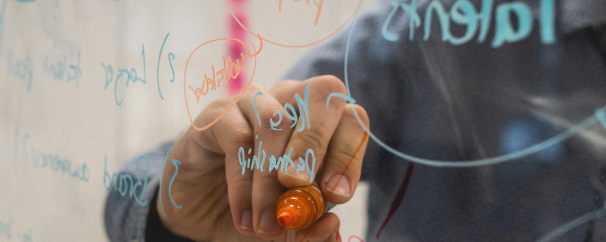 Persona escribiendo ideas de negocio en una pizarra de cristal durante una sesión de brainstorming