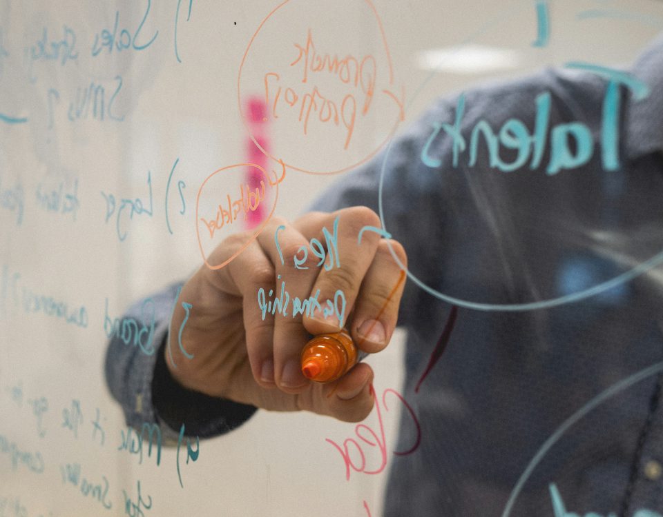 Persona escribiendo ideas de negocio en una pizarra de cristal durante una sesión de brainstorming